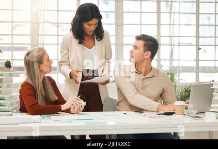 African american businesswoman talking about a document with colleagues. Team of designers collaborate and brainstorm. Diverse businesspeople planning Stock Photo