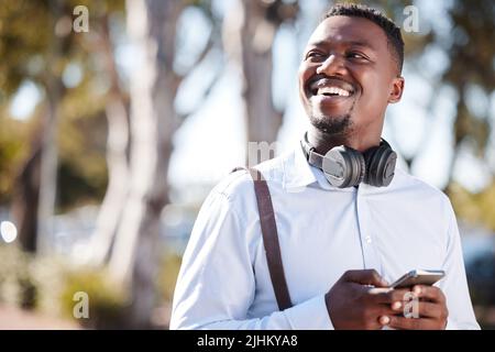Happy african american businessman wearing headphones and texting on a cellphone while commuting in the city. One young black guy looking thoughtful Stock Photo