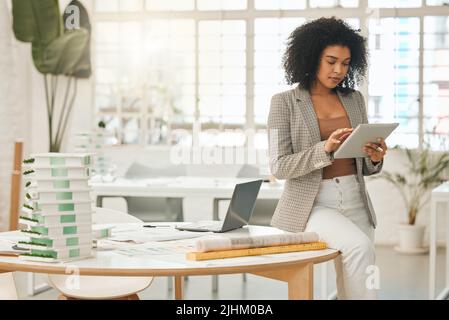 Leading businesswoman using a digital tablet. Creative entrepreneur using an online app. Young architect working in her agency. Focused businesswoman Stock Photo
