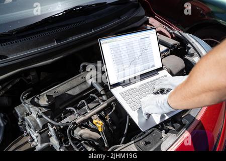 Young Male Mechanic Using Laptop While Examining Car Engine Stock Photo