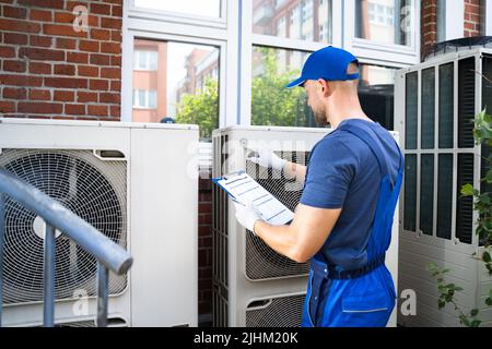 Two Electricians Men Wearing Safety Jackets Checking Air Conditioning Unit On Building Rooftop Stock Photo