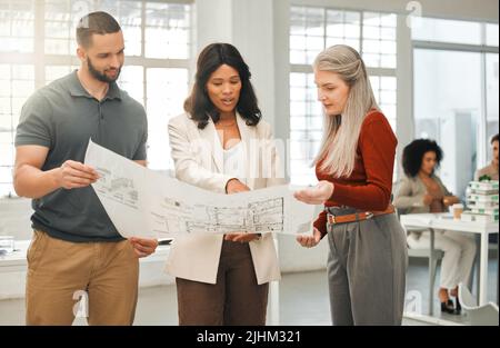 Engineers looking at a blueprint. Diverse businesspeople looking at a building plan. Mature businesswoman collaborating with staff. Architects Stock Photo