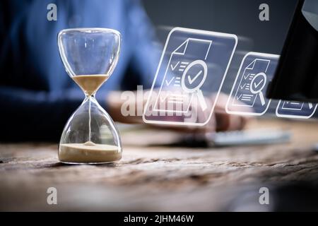 Close-up Of Hourglass In Front Of Businessperson's Hand Calculating Invoice Stock Photo