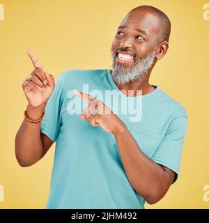 Mature african man smiling and pointing in a direction against a yellow studio background. Black guy looking happy and making a pointing gesture Stock Photo