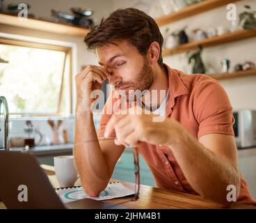 Young caucasian businessman suffering from a headache while working on a laptop from home alone. One stressed man looking unhappy while using a laptop Stock Photo