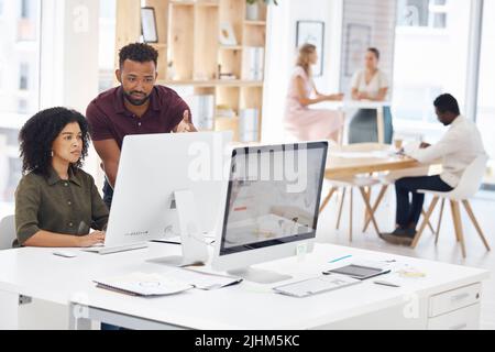 Two happy mixed race businesspeople working on a computer in an office at work. Cheerful hispanic colleagues using a desktop computer together Stock Photo