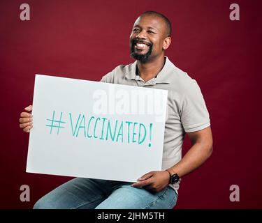 African american covid vaccinated man showing and holding poster. Smiling black man isolated against red studio background with copyspace. Happy model Stock Photo