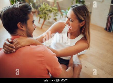 Funny young caucasian couple being playful laughing and having fun while sitting together at home. Young woman sitting on boyfriends lap putting her Stock Photo