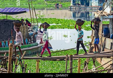 Women workers carrying baskets filled with coal on their head in the Gabtoli region of Dhaka Stock Photo