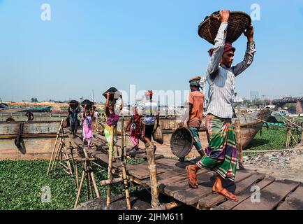 Women workers carrying baskets filled with coal on their head in the Gabtoli region of Dhaka Stock Photo