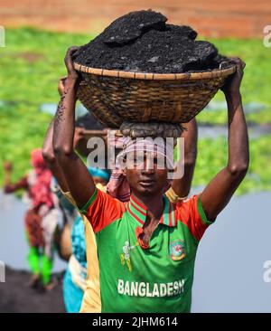 Women workers carrying baskets filled with coal on their head in the Gabtoli region of Dhaka Stock Photo