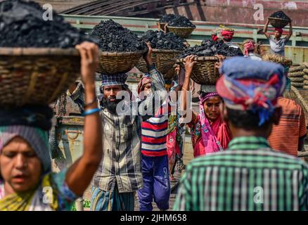 Women workers carrying baskets filled with coal on their head in the Gabtoli region of Dhaka Stock Photo