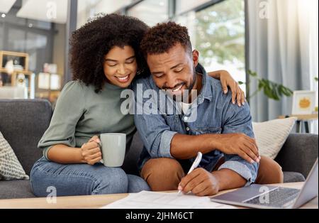 Young mixed race couple going through bills and using a laptop at a table together at home. Husband and wife planning and working on documents Stock Photo