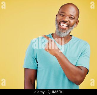 Mature african man laughing and pointing in a direction against a yellow studio background. Black guy giggling and making a pointing gesture reacting Stock Photo