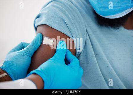 Closeup of doctor applying a plaster on the arm of a patient. Hand of a medical gp as they apply a plaster cropped. African american doctor applying a Stock Photo