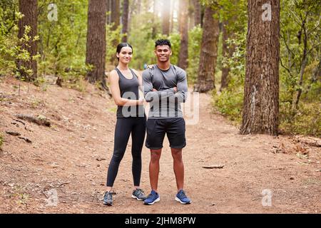 Full length portrait of a happy fit young couple standing with their arms crossed wearing sportswear and ready for a run in nature. Young female and Stock Photo