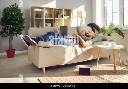 Happy young man relaxing on the couch at home and watching a movie on his laptop Stock Photo