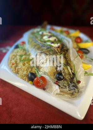 whole fish baked pike perch on a white platter is served in the restaurant. Stock Photo