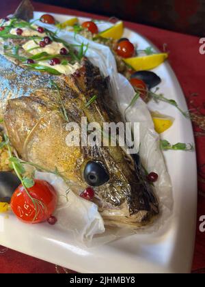 whole fish baked pike perch on a white platter close-up. Stock Photo