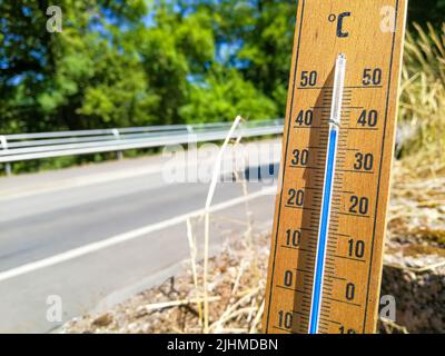 Detail of thermometer shows high temperature of over 35 in summer against trees and cloudless sky with focus on thermometer Stock Photo