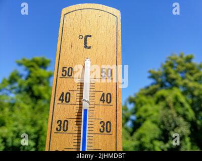 Detail of thermometer shows high temperature of over 35 in summer against trees and cloudless sky with focus on thermometer Stock Photo