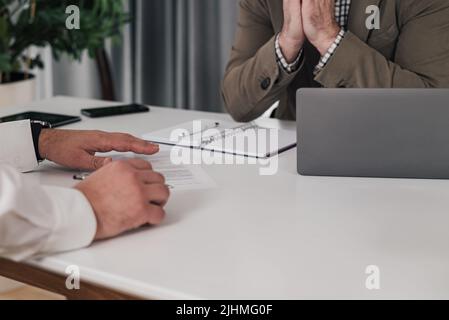 Male colleague sitting with laptop computer, senior entrepreneur examining papers at the desk. They are sitting in office and brainstorming. Stock Photo