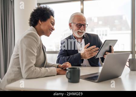 Senior businessman explaining strategy to female coworker. Professionals are discussing over digital tablet at desk. They are wearing formals in offic Stock Photo