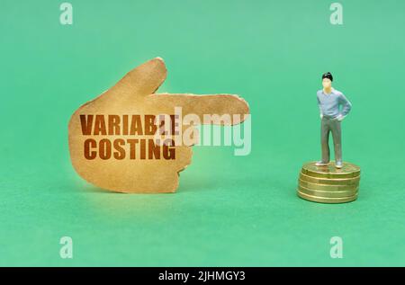 Business concept. On the green surface on the coins there is a figure of a man, a hand with the inscription points to him - Variable Costing Stock Photo