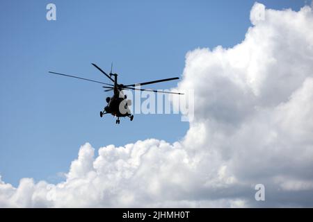 Silhouette of military helicopter Mi-8 (NATO codification: Hip) in flight on background of blue sky and white clouds Stock Photo