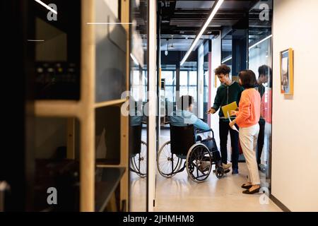 Multiracial colleagues discussing with businessman sitting in wheelchair at office corridor Stock Photo