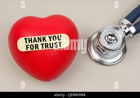 Medicine concept. Near the stethoscope lies a heart on which a sticker is pasted with the inscription - Thank you for trust Stock Photo