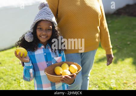 Image of happy african american girl with grandmother holding bowl with lemons Stock Photo