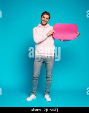 Image of emotional excited young man posing isolated over light blue wall background holding speech bubble Stock Photo
