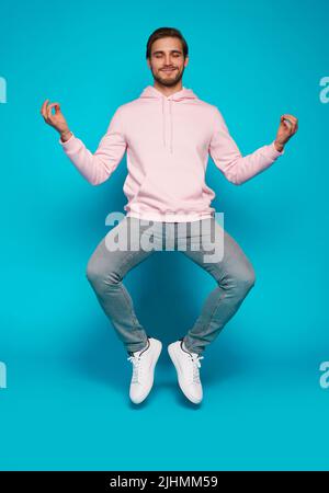 Full length of focused minded thoughtful man sitting doing yoga while jumping up isolated on light blue color background Stock Photo