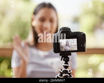 Blogging is my passion. a young woman sitting alone outside and using her camera to vlog. Stock Photo