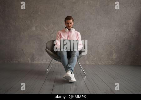 Handsome Young Freelancer Guy Using Laptop While Sitting In Arnchair At Home, Millennial Man Working Online On Computer Stock Photo