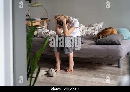 Unhappy woman sitting on sofa holding head in hands suffering from hangover headache in morning Stock Photo