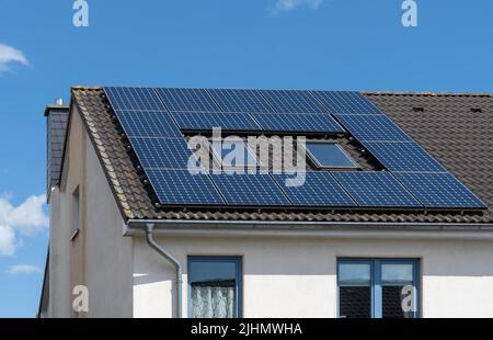 solar panels of a photovoltaic power plant on the roof of a black tiled house Stock Photo