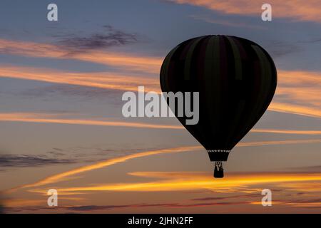 A hot air balloon is silhouetted against the sky at sunset in a composite image. Stock Photo