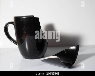 Broken black porcelain coffee cup on a white background Stock Photo