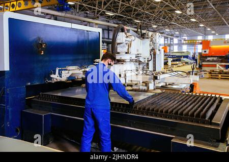 Worker puts steel sheet into loading unit of cutting machine. Stock Photo