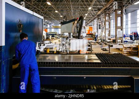 Worker puts steel sheet into loading unit of cutting machine. Stock Photo
