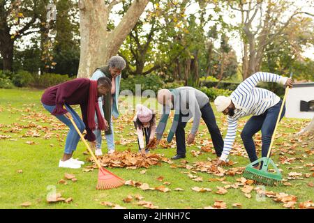 Image of happy african american multi generation family swiping leaves in autumn garden Stock Photo
