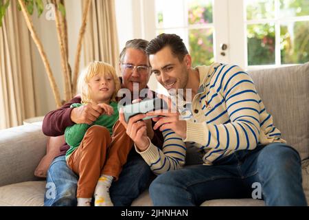 Image of happy three generation caucasian men sitting on sofa and using smartphone Stock Photo