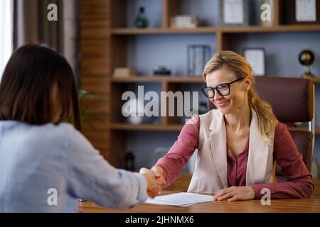 Two business women shaking hands. Successful conclusion of an agreement with the client or customer, making business deal at office meeting. Applicant Stock Photo
