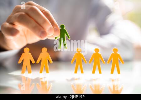 Businessperson's Hand Picking Red Human Figures Amongst Blue Figures In A Row Stock Photo