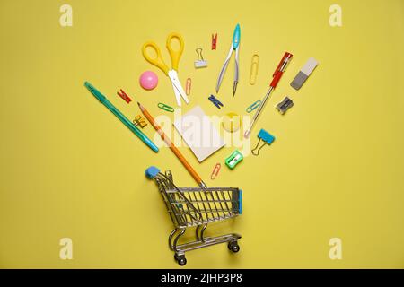 Trolley cart with school supplies on a yellow background. Flat, top view. Back to school concept. Stock Photo