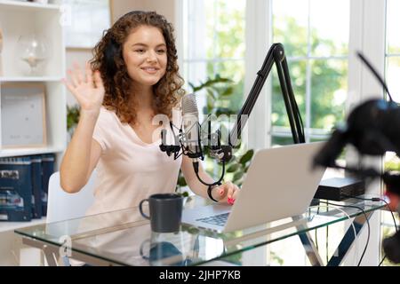 Woman vlogger with headphones looking at laptop and recording video on professional camera Stock Photo