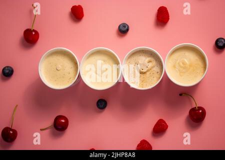 An assortment of four cans of Italian ice cream gelato stands on pink table, scattered cherries, raspberries, blueberries berries. A mouthwatering, co Stock Photo