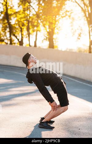 Man stretching on stadium in evening, sunset light Stock Photo